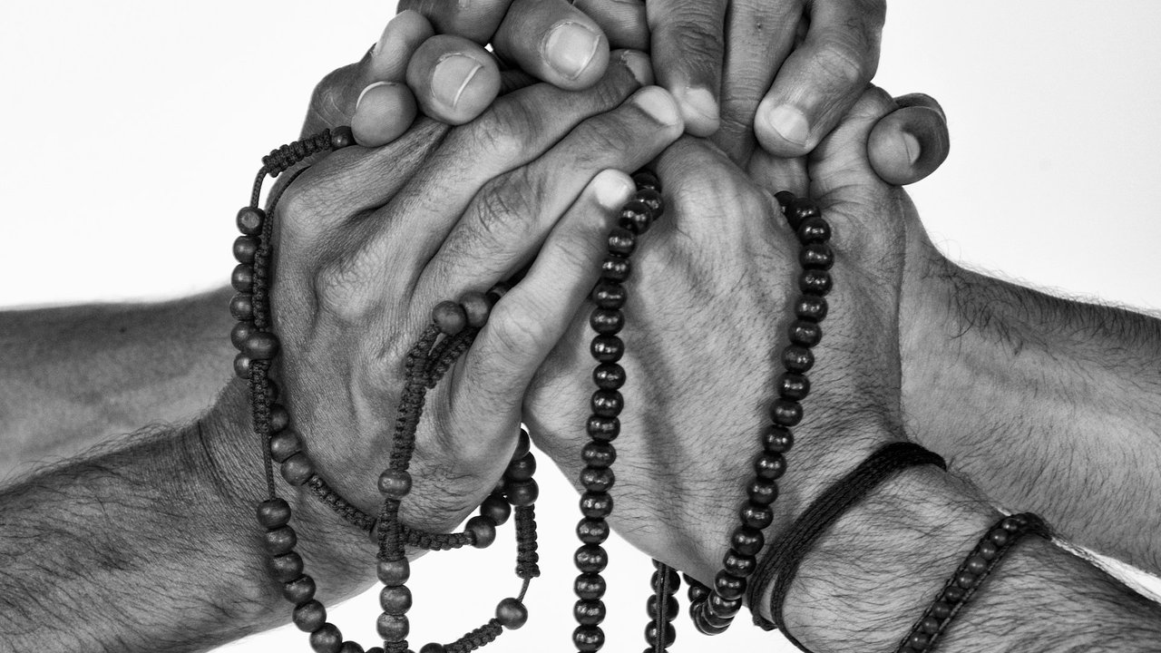 Drei Hände mit Gebetsuntensilien aus Islam, Judentum und Christentum im gemeinsamen Gebet
