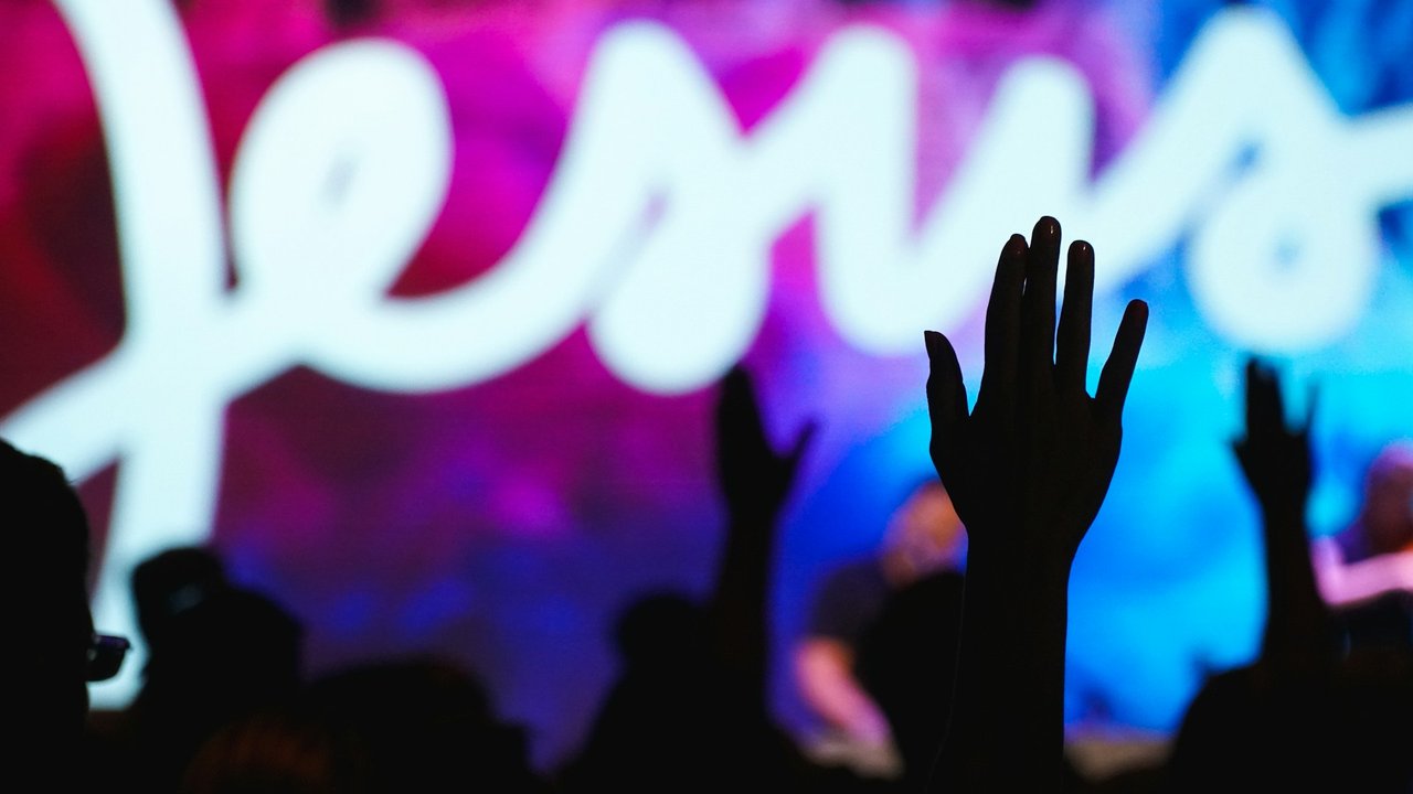 Viele Menschen mit erhobenen Menschen. Im Hintergrund ist auf einer Bühne das Wort Jesus zu lesen.